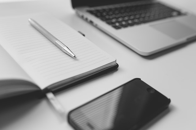 desk with laptop, cellphone, pen and paper on it